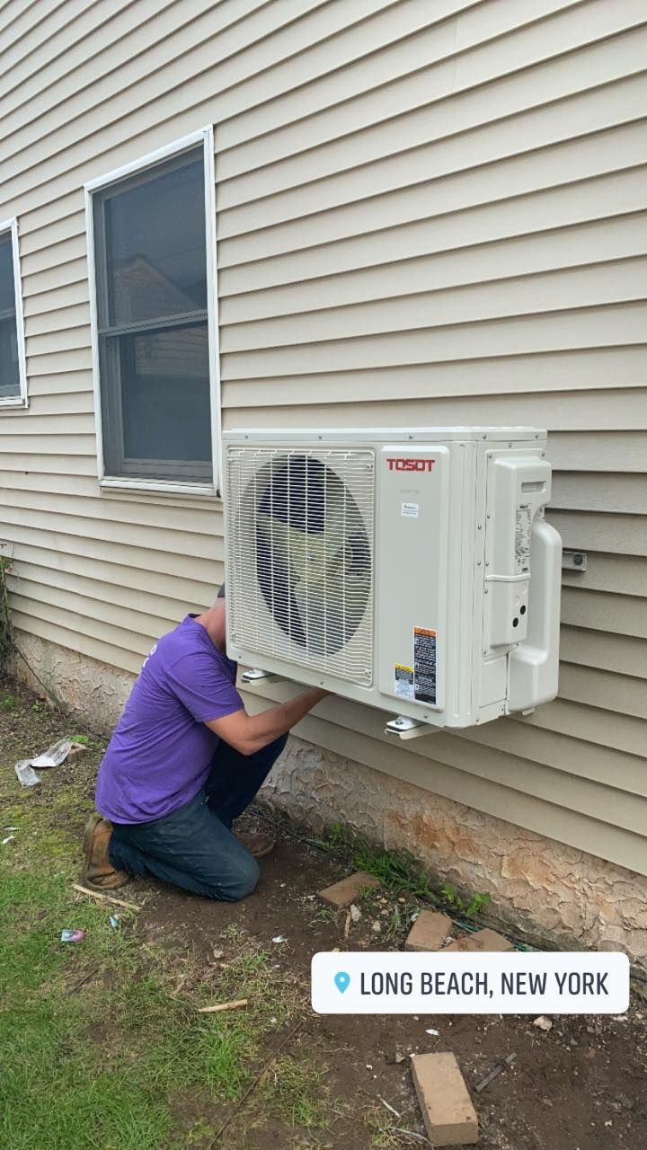 A man is installing an air conditioner on the side of a house.