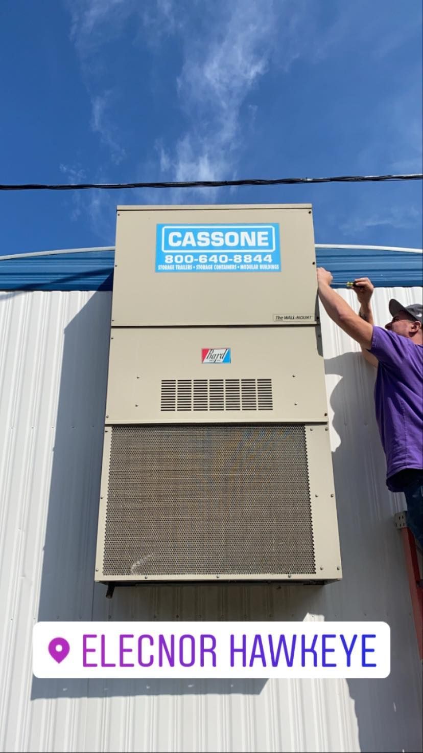 A man is installing a cassone air conditioner on the side of a building.