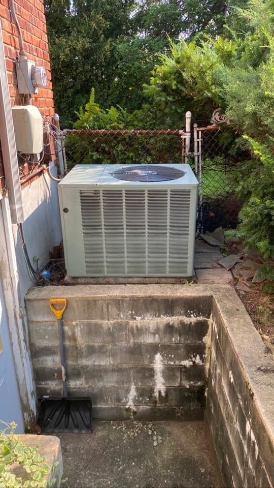 An air conditioner is sitting on top of a concrete wall next to a shovel.