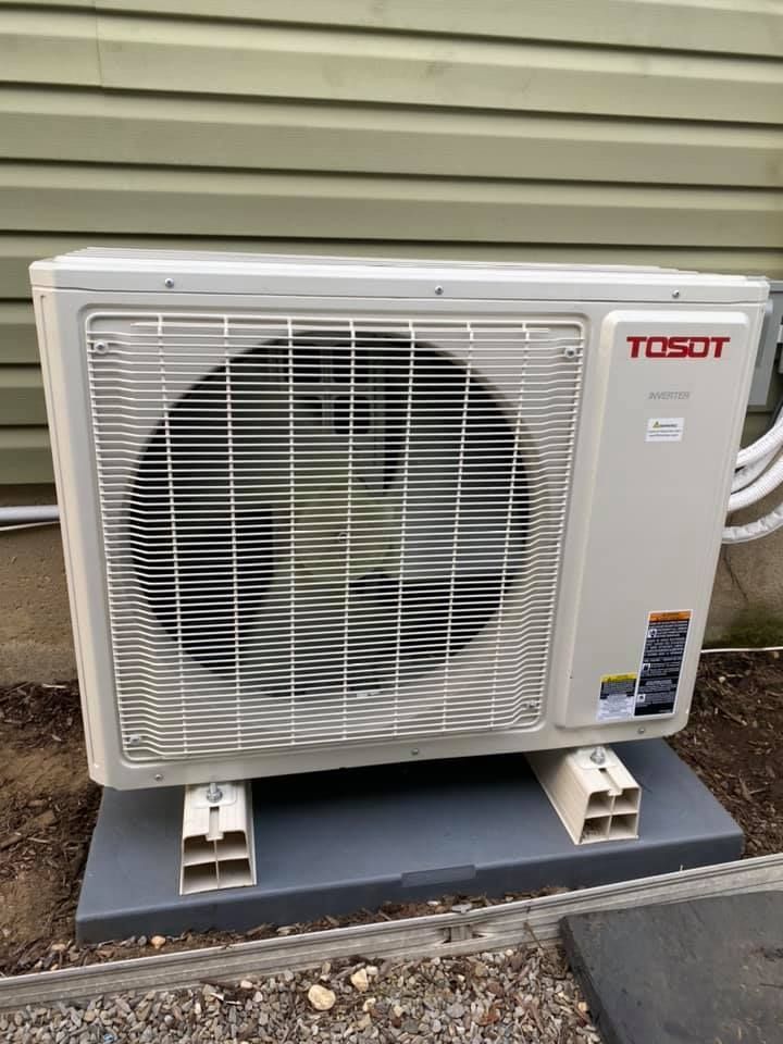 A togot air conditioner is sitting on top of a concrete platform outside of a house.