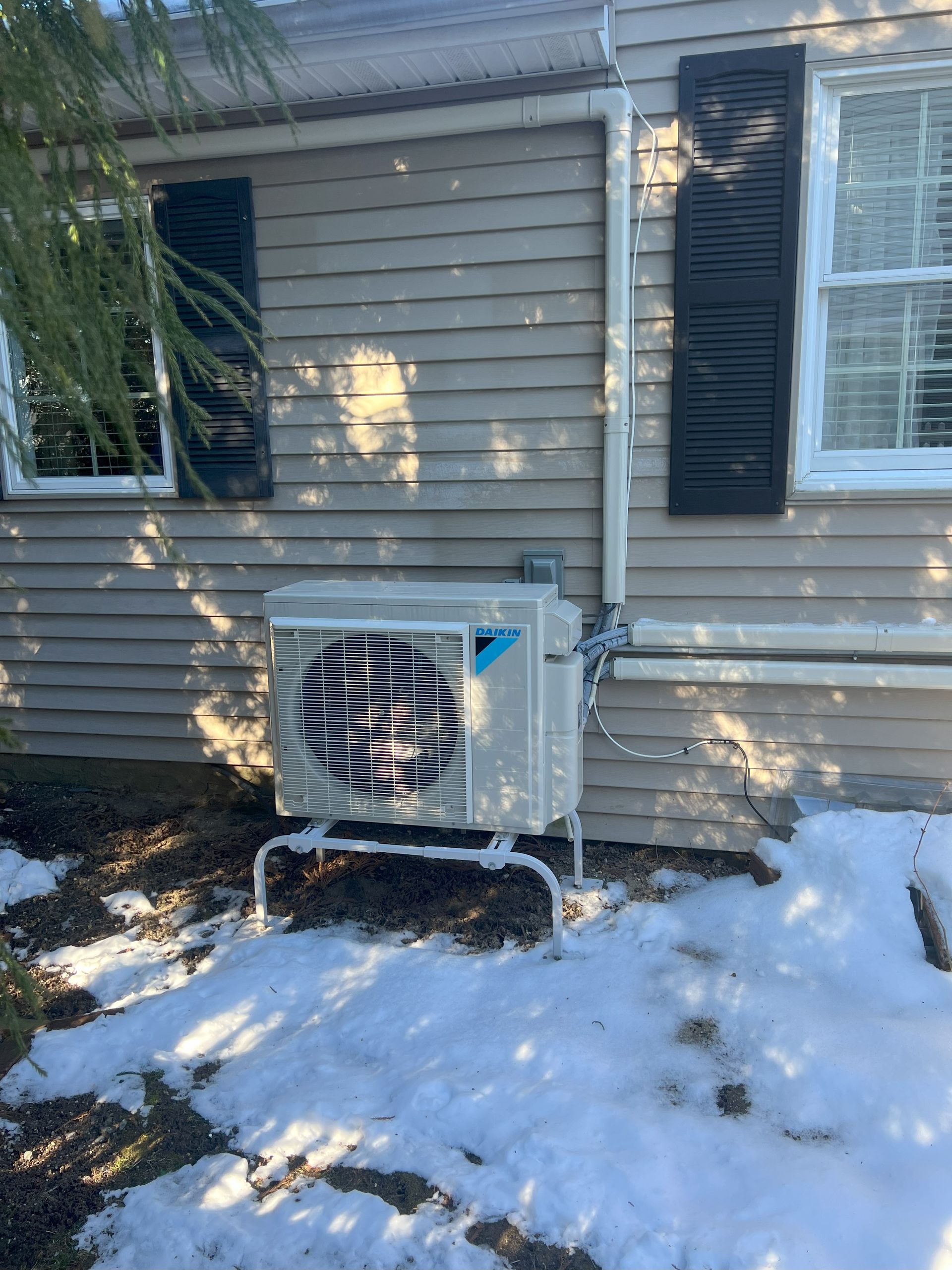 A white air conditioner is sitting on the side of a house in the snow.