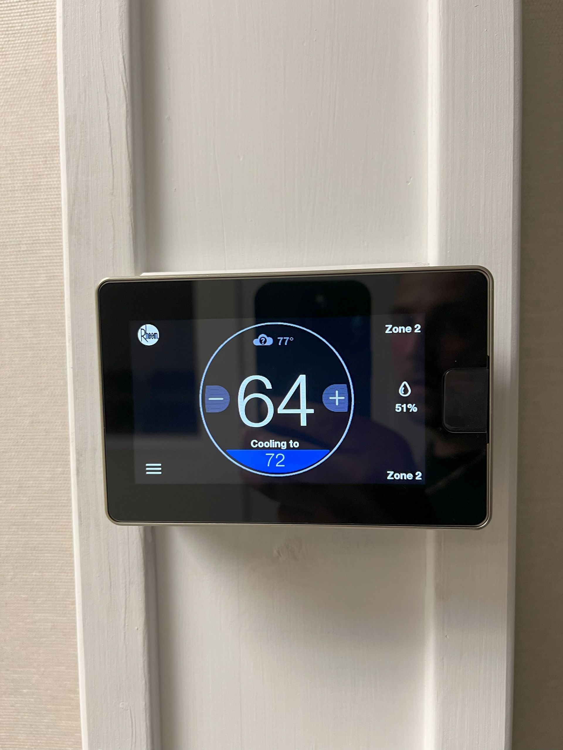 A smart thermostat is hanging on a white wall.