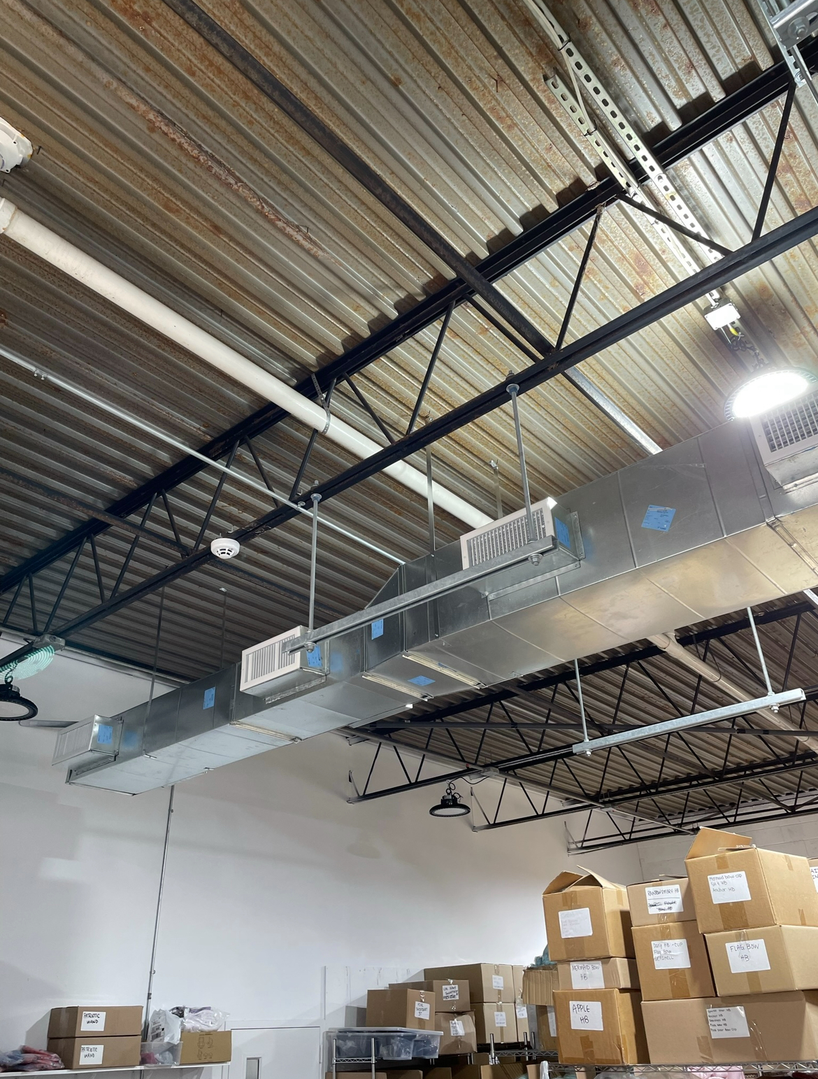 A warehouse with boxes stacked on top of each other and a large air duct hanging from the ceiling.