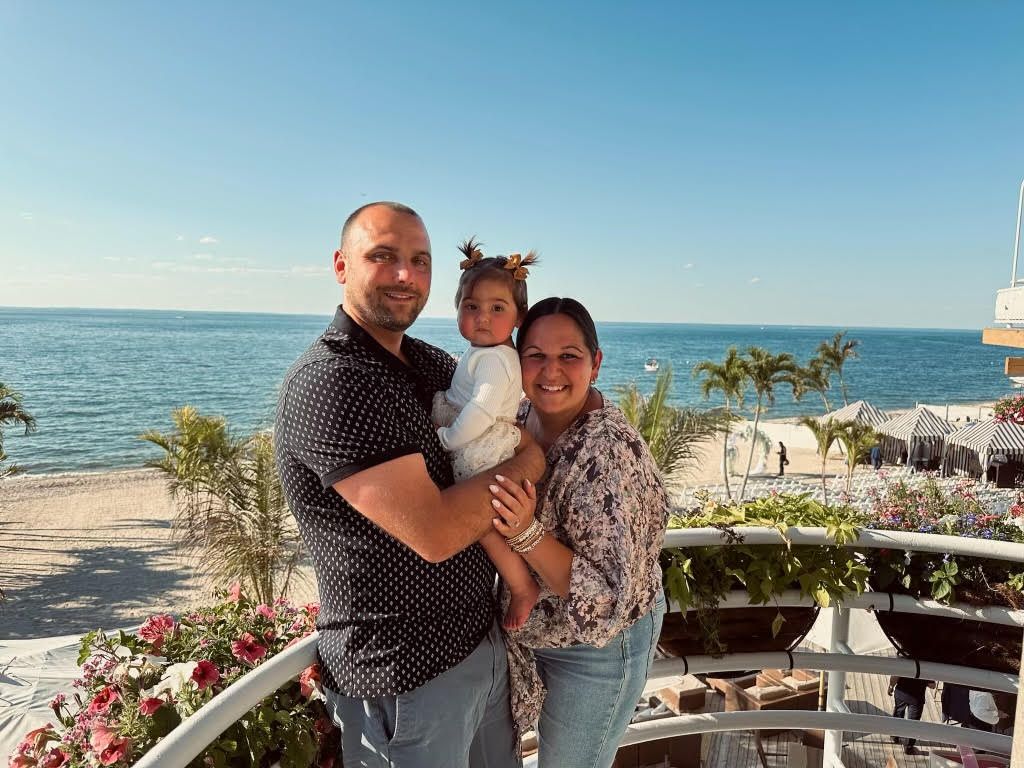 A man and woman are holding a little girl on a balcony overlooking the ocean.