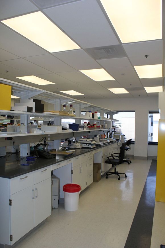 Person wearing a mask vacuuming a lab floor with a backpack vacuum cleaner.