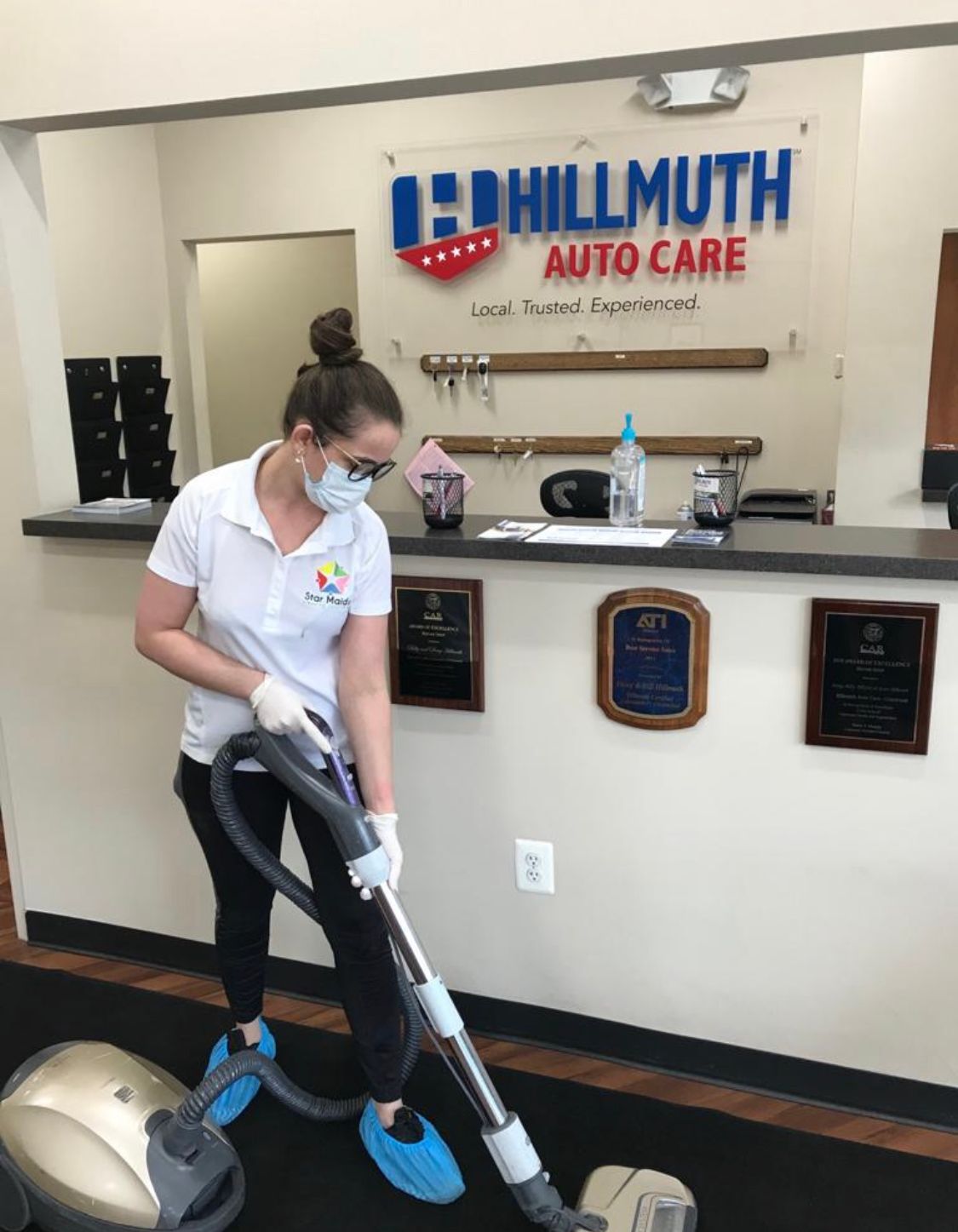 Person vacuuming floor inside Hillmuth Auto Care wearing mask and gloves. Person vacuuming floor inside Hillmuth Auto Care wearing mask and gloves.