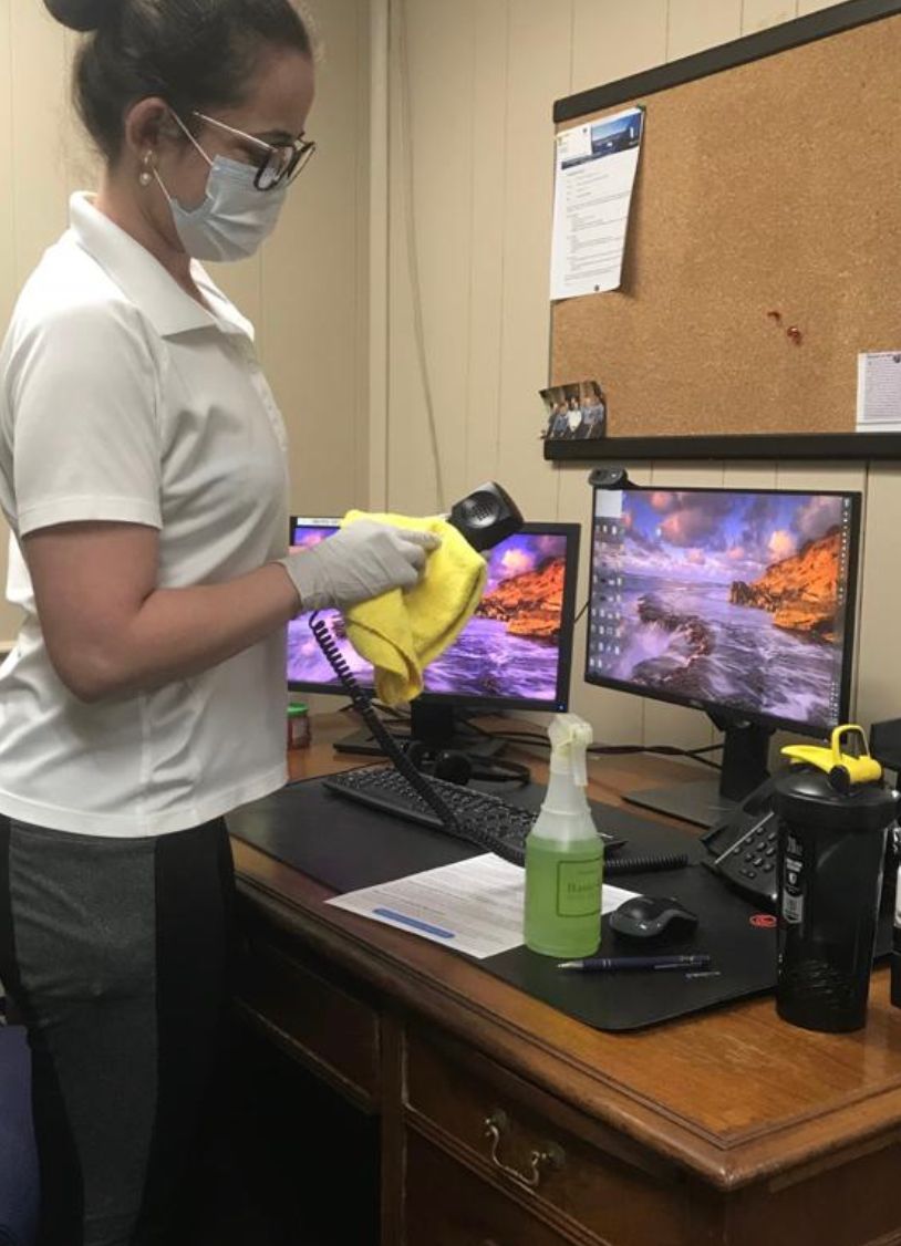 Person wearing mask and gloves disinfecting a desk with a spray bottle and steamer. Person wearing mask and gloves disinfecting a desk with a spray bottle and steamer.