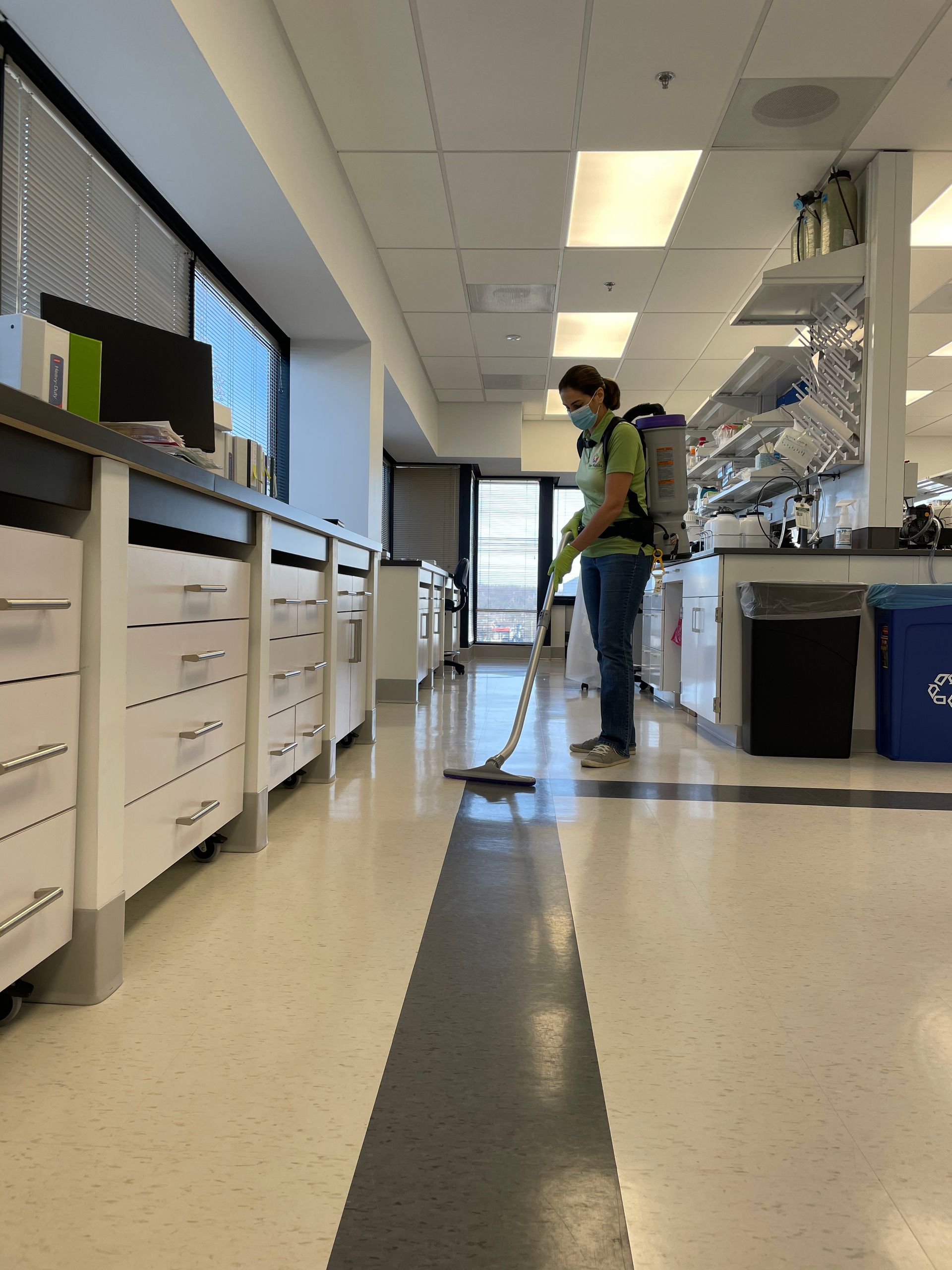 Person wearing a mask and backpack sprayer cleaning a lab floor.