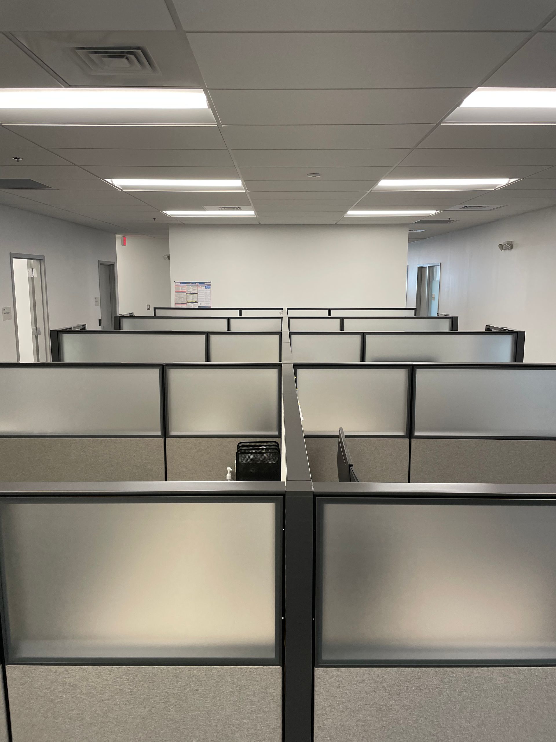 An empty office space with rows of cubicles under bright overhead lights.