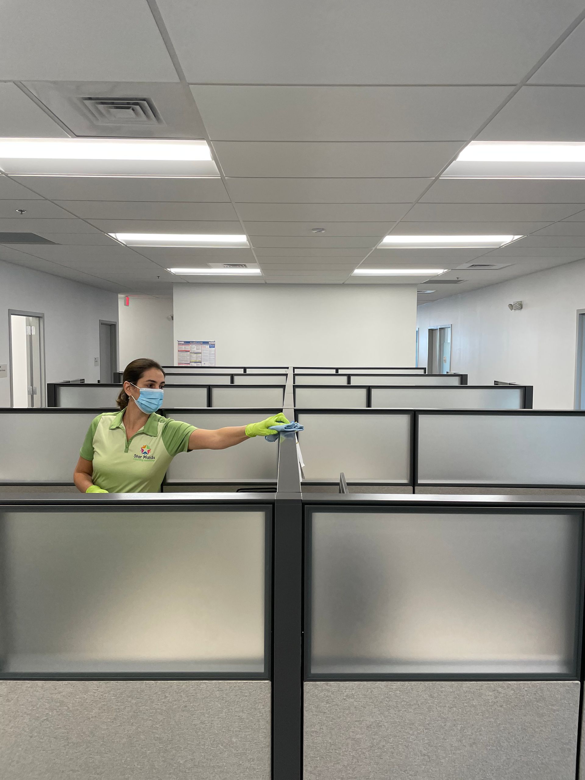 Person wearing mask and gloves sprays partition in an empty office.