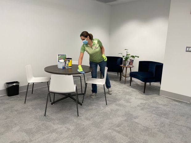Person wearing a face mask and gloves cleaning a table in a waiting room.