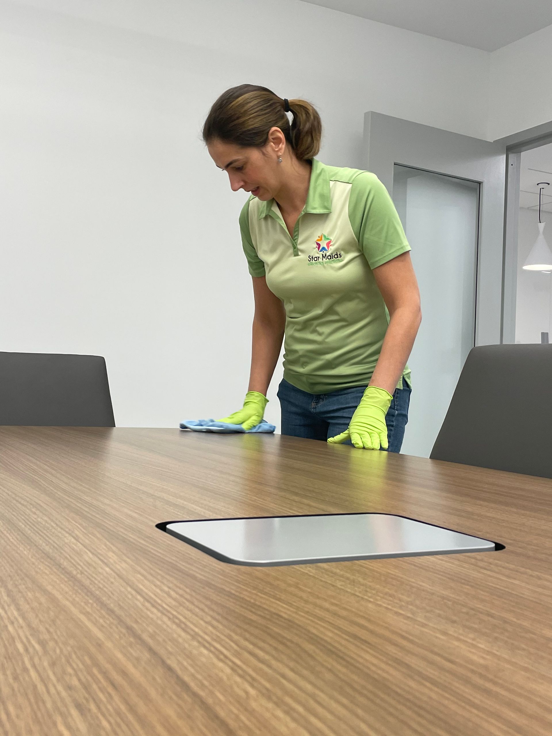 Person wearing gloves cleaning a wooden table in an office setting.