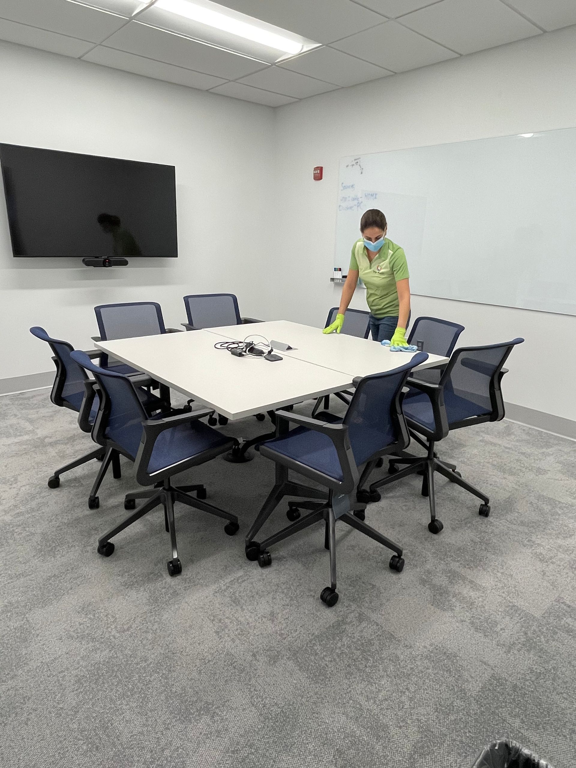 Person wearing gloves cleaning a white conference table in a modern office.