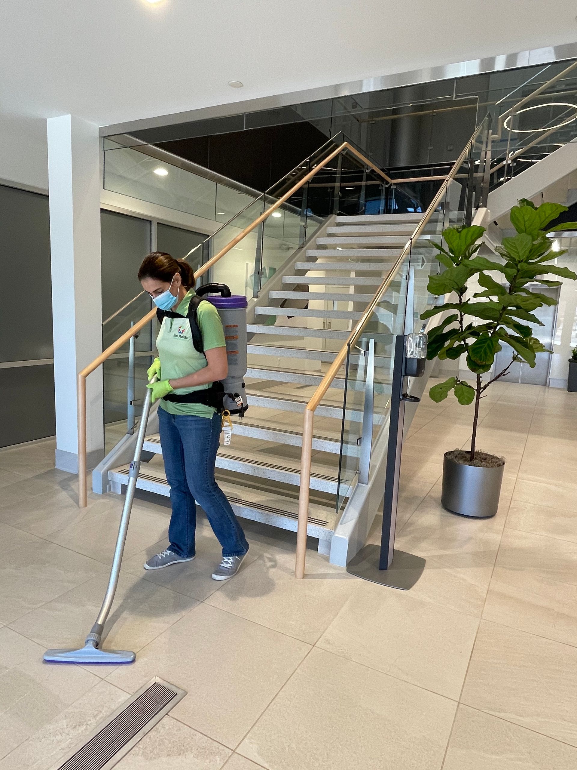 Person with backpack vacuum cleaning floor near stairs and a potted plant.