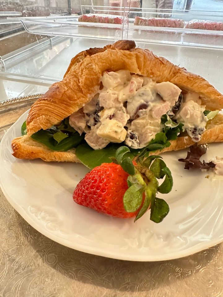 A chicken salad sandwich on a croissant with a strawberry on a white plate.