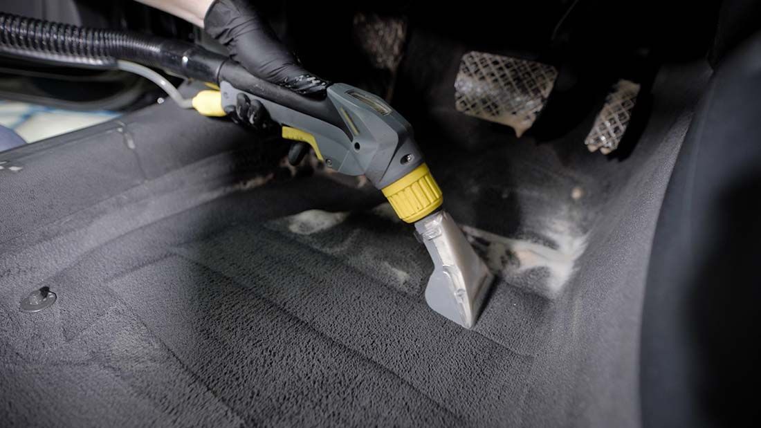 A person is cleaning the floor of a car with a vacuum cleaner.