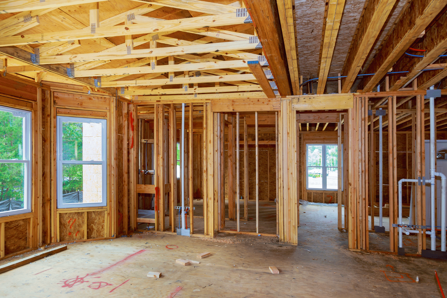 Interior of a wooden house under construction, showing framing, windows, and exposed beams.