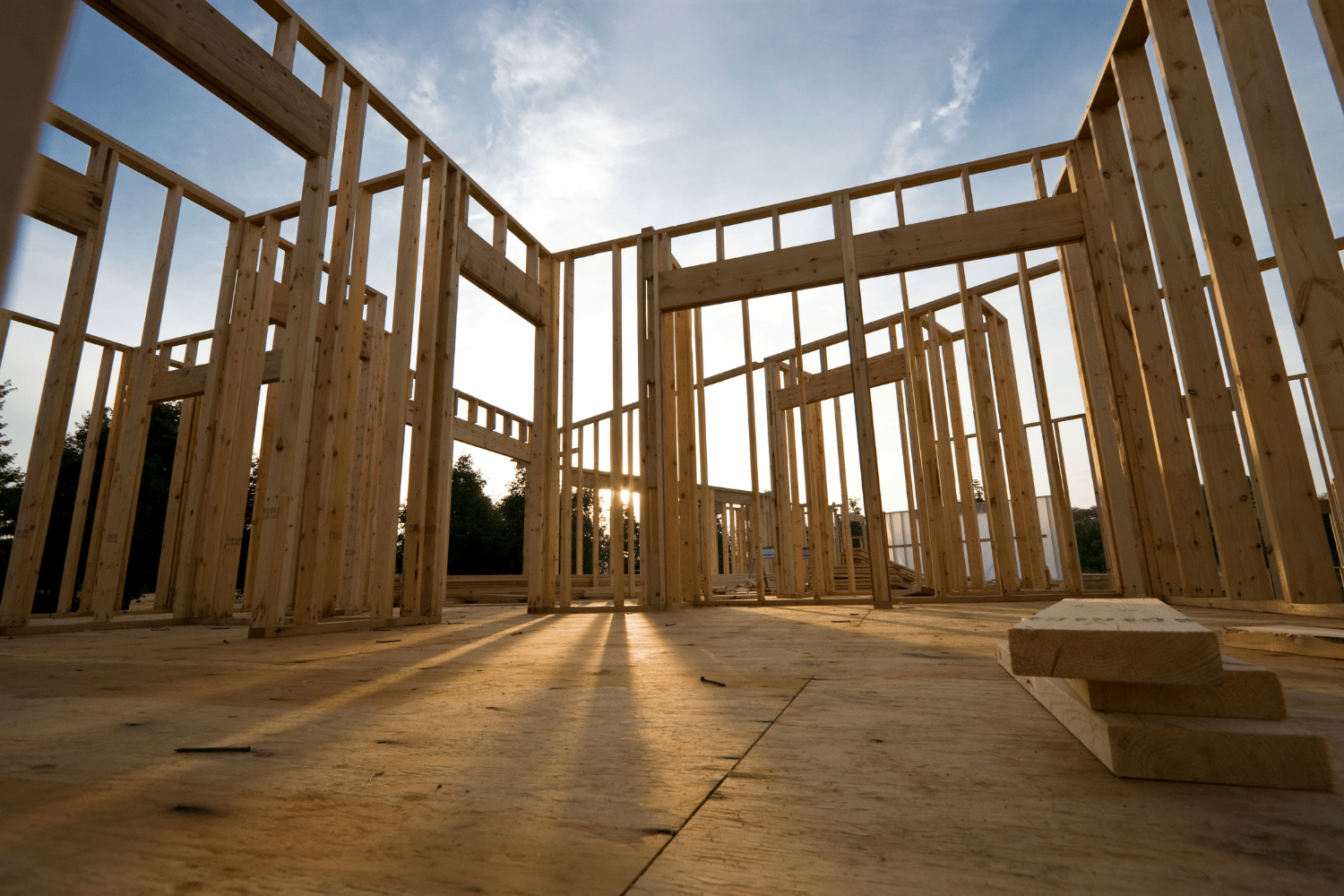 Wooden frame of a house under construction; sunlight streams through the open structure.