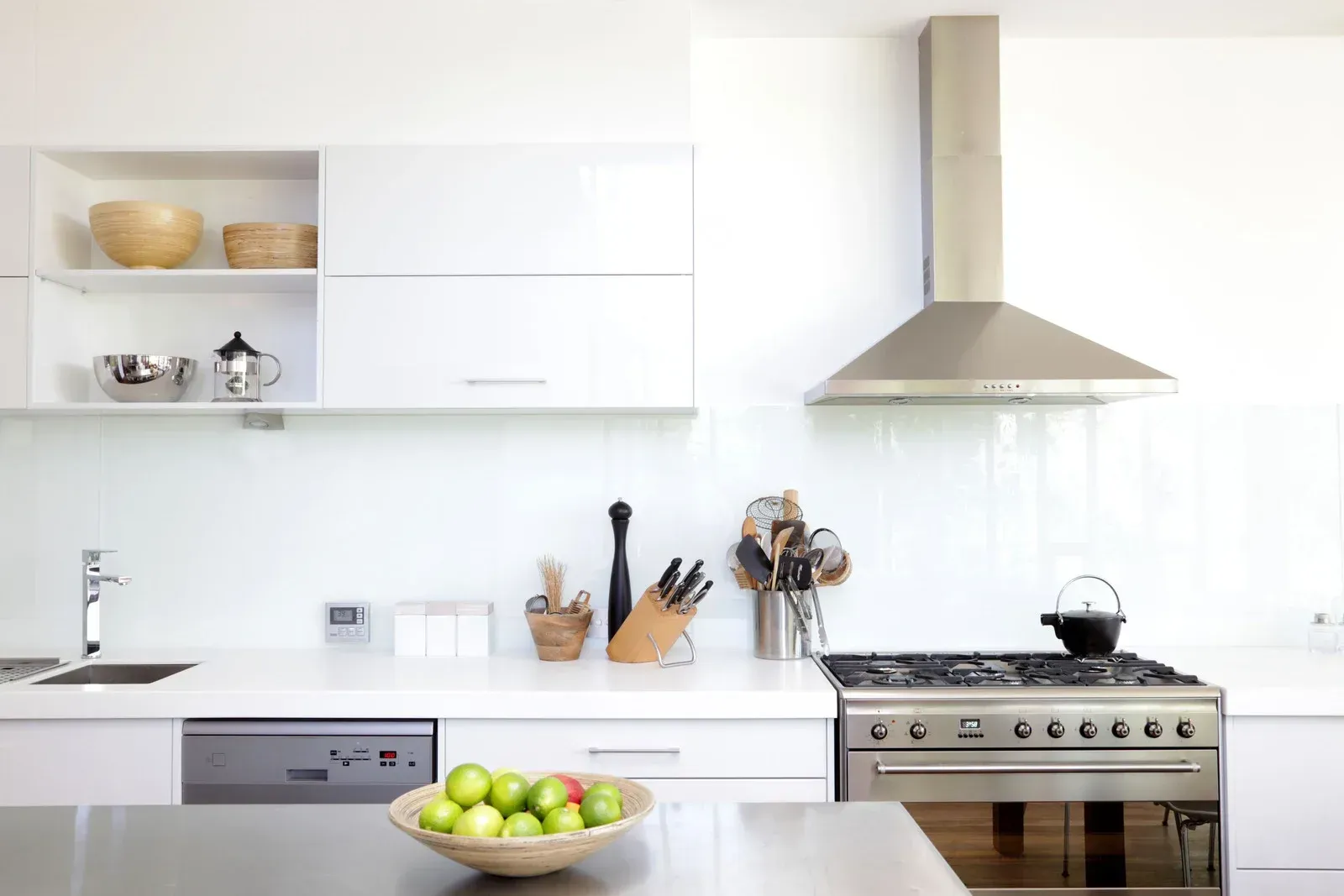 Modern white kitchen with stainless steel appliances, a bowl of green apples, and a range hood.