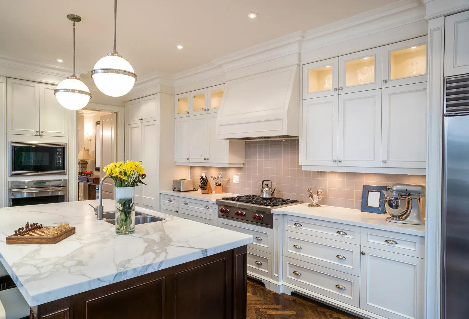 A kitchen with white cabinets , marble counter tops , stainless steel appliances and a large island.