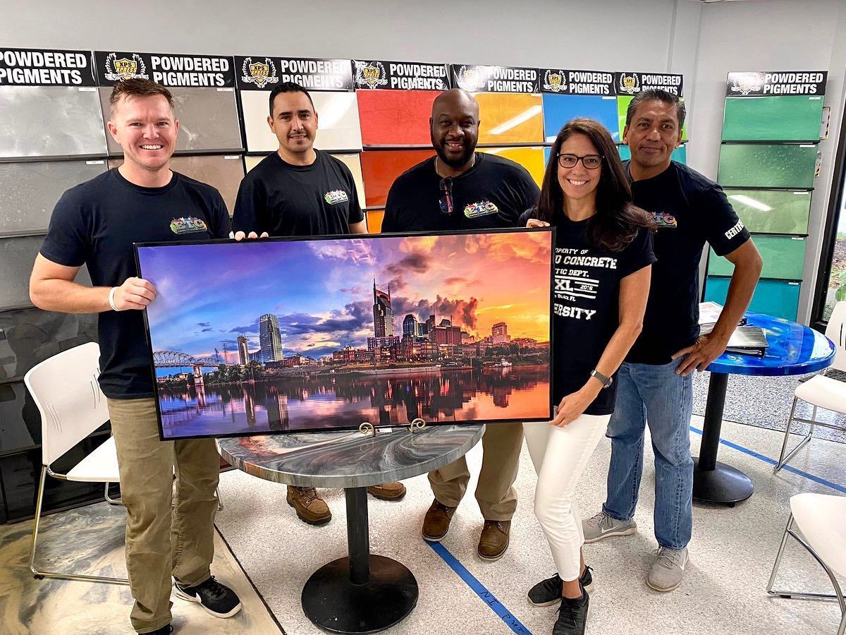 A group of people are standing around a table holding a large painting.