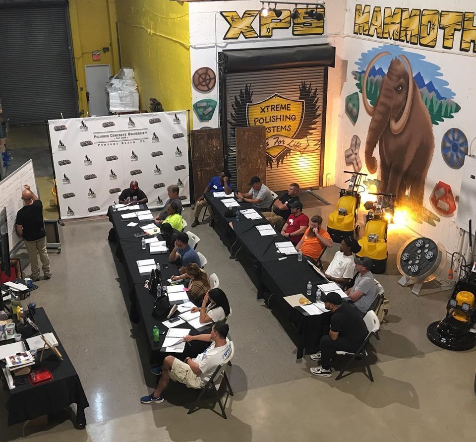 A group of people are sitting at long tables in front of a wall that says xpe mammoth