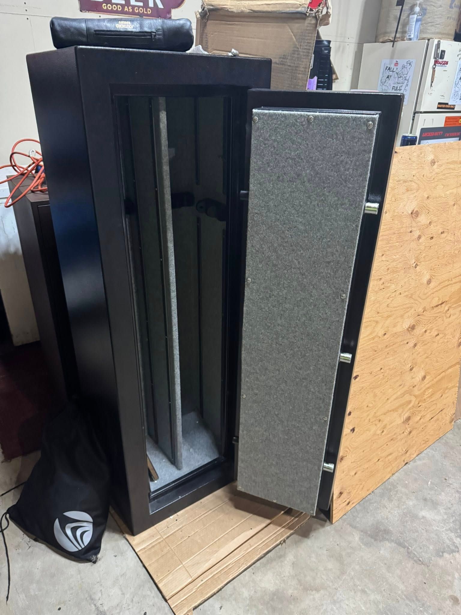 Black gun safe with open door, revealing interior storage. It is set up indoors on cardboard.