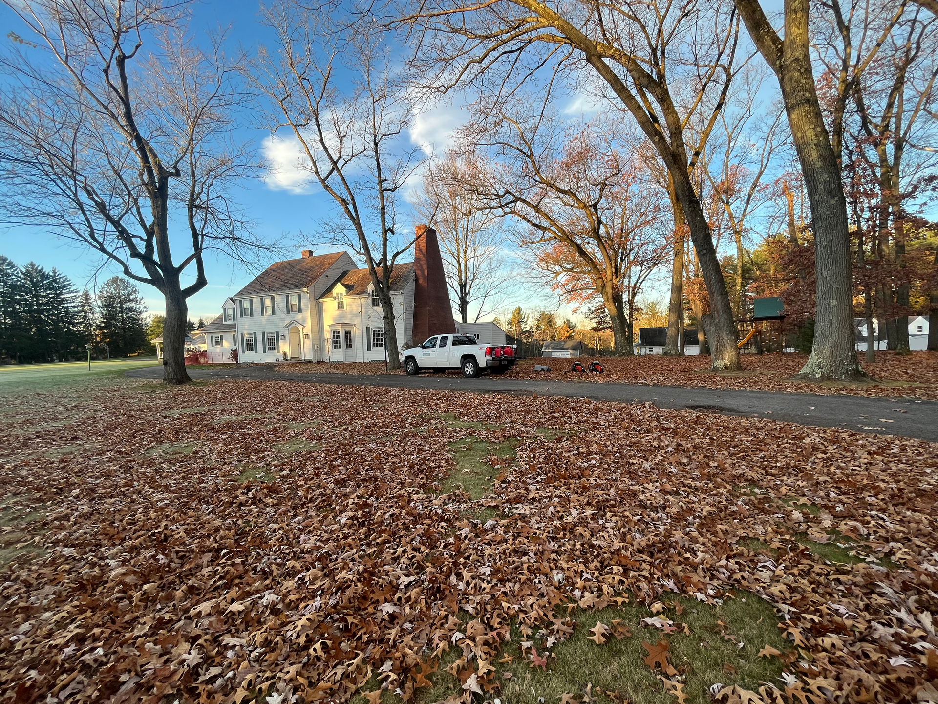 a white truck is parked in front of a house surrounded by leaves .