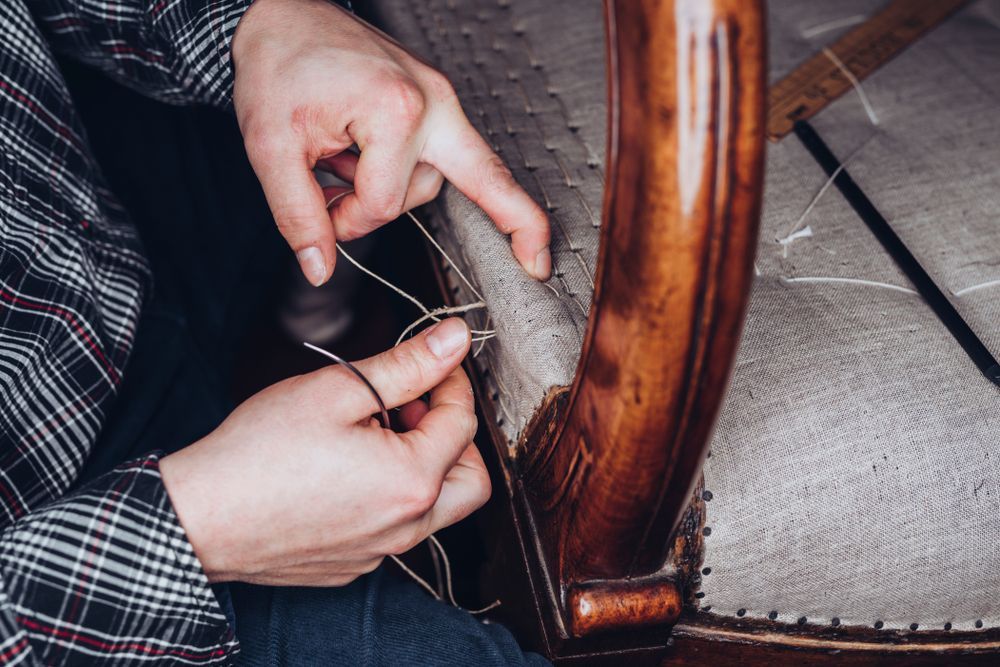 Person's Hands Sewing Fabric onto A Wooden Chair Frame, Showing the Restoration of A Seat — Instyle Curtains & Blinds In Bungalow, QLD