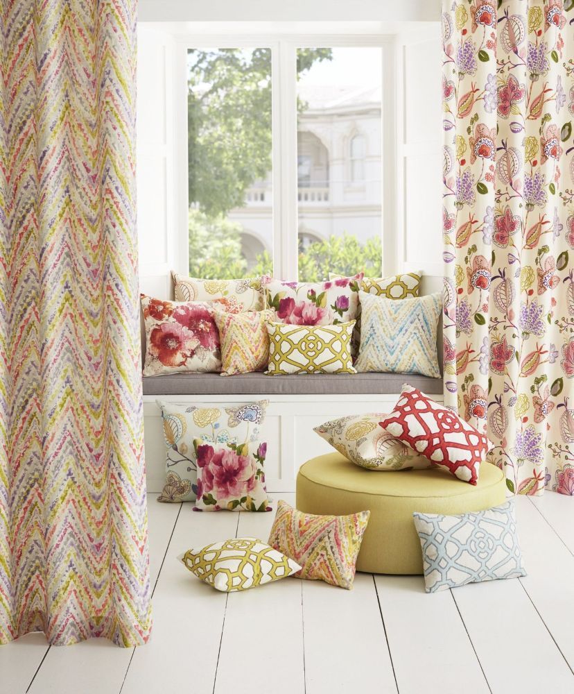 A cushion-covered bench in front of a window. Either side has a curtain with floral patterns.