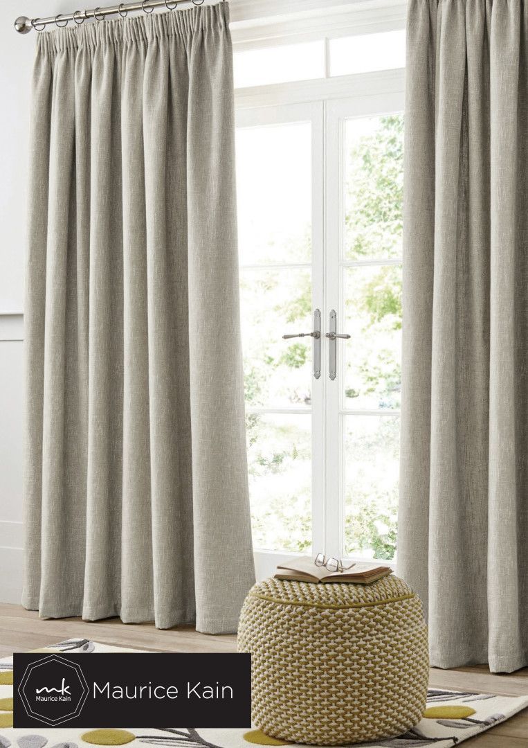 Beige curtains framing a white door; a woven ottoman sits on a patterned rug.