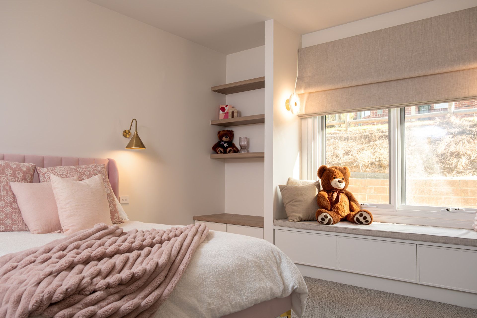 Bedroom with pink bed, window seat, built-in shelves, and a teddy bear.