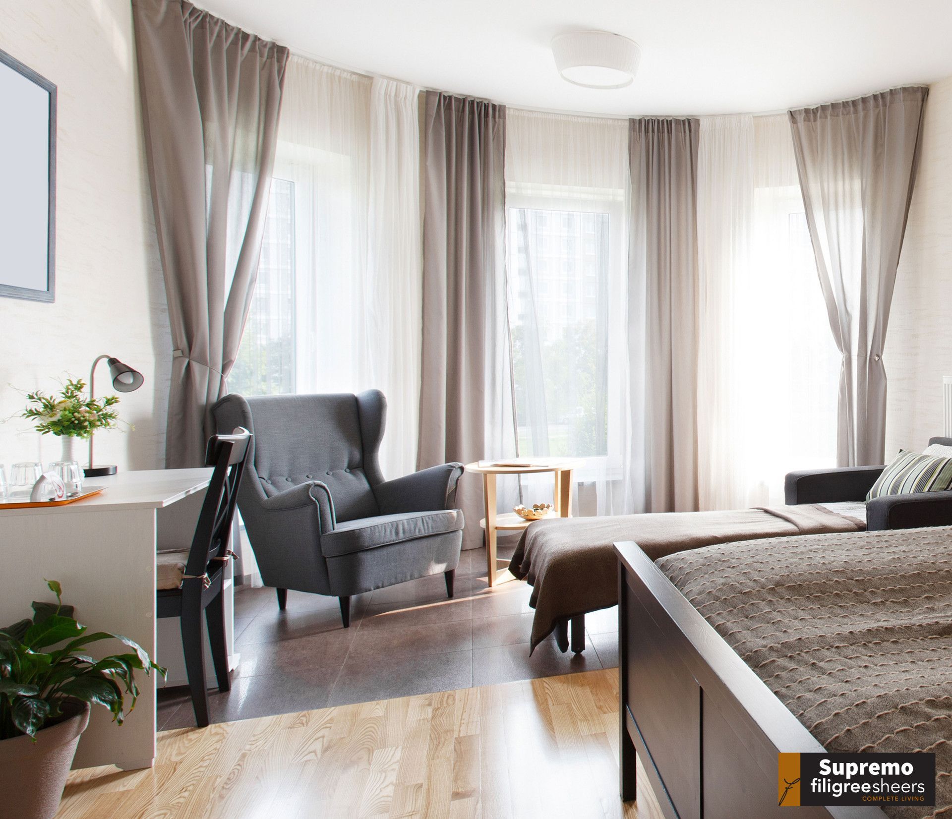 Hotel room with curved wall, windows, chair, desk, beds, and curtains.