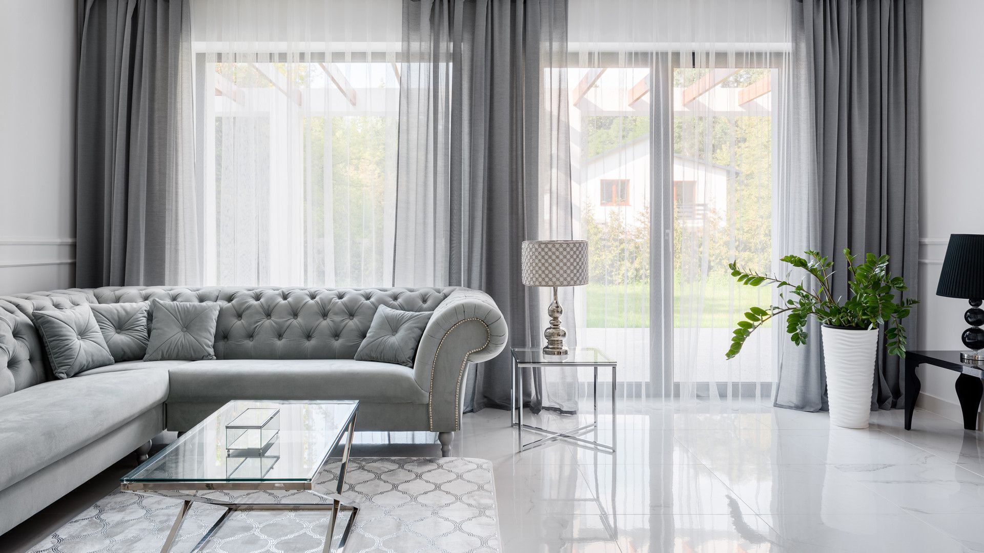 Gray living room with a tufted sectional sofa, sheer curtains, and a glass-topped coffee table.