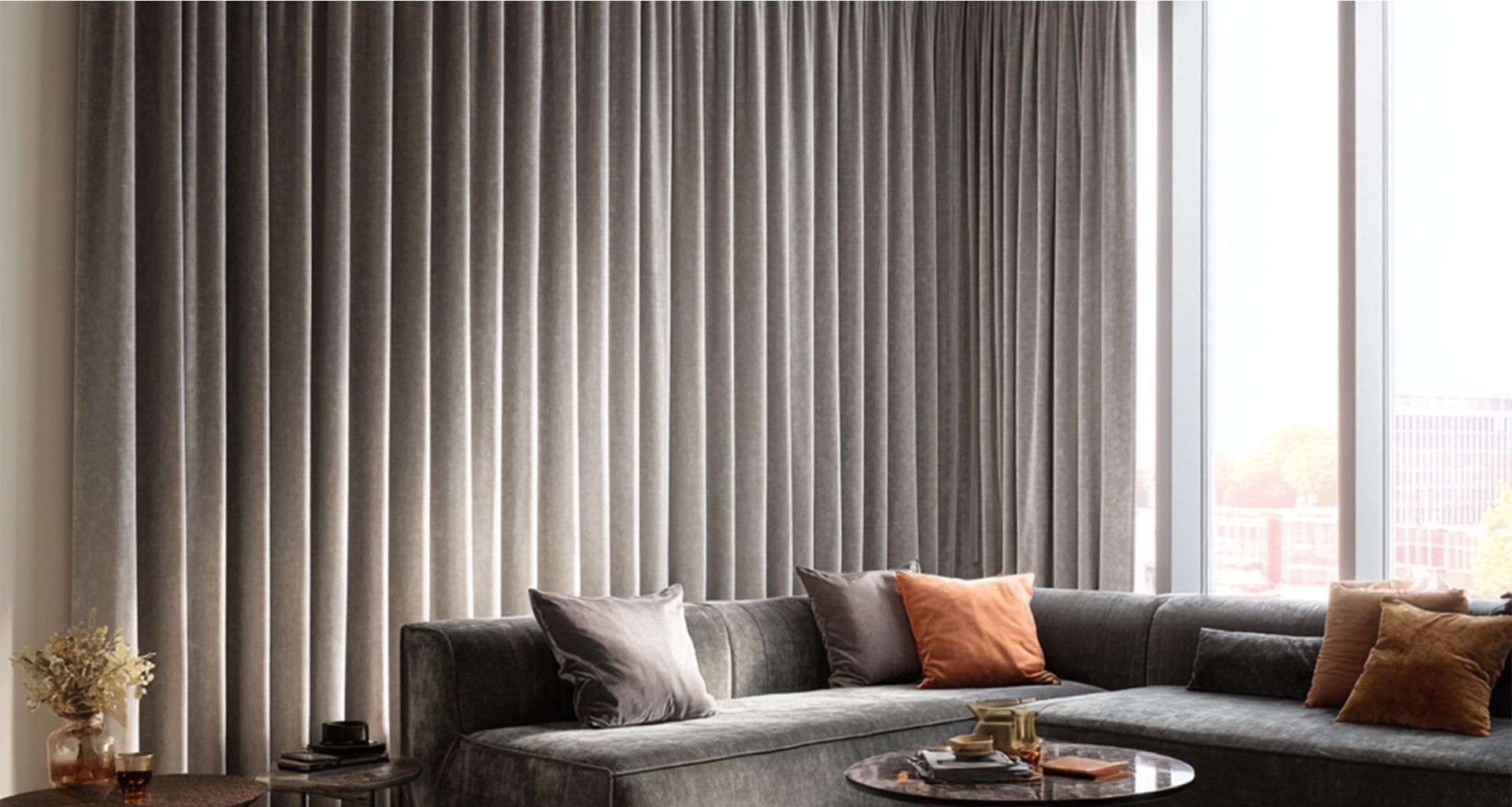Living room with gray velvet sectional, sheer curtains, and throw pillows in earth tones.