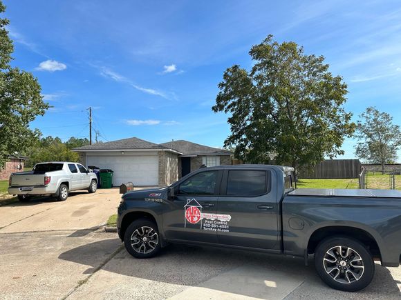A grey pickup truck with a company logo parked in a residential driveway in front of a house on a sunny day.