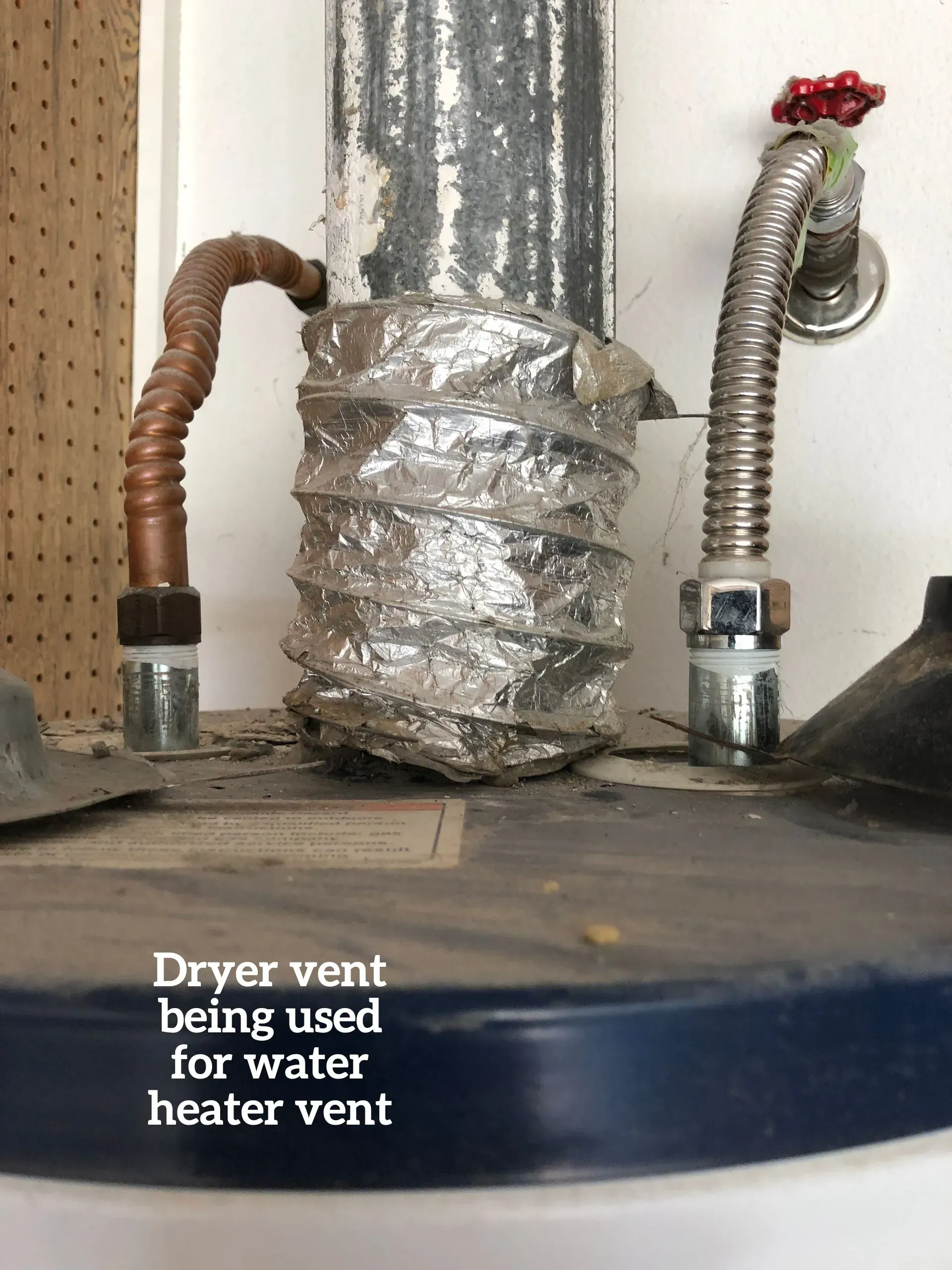 A water heater top showing a flexible, silver foil dryer vent pipe improperly connected to the flue vent.