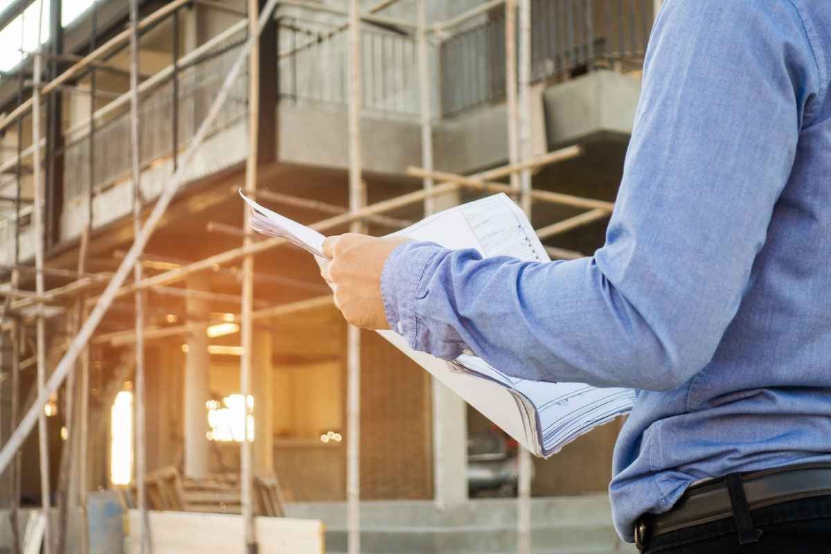 A person in a blue shirt holds blueprints at a construction site with wooden scaffolding.