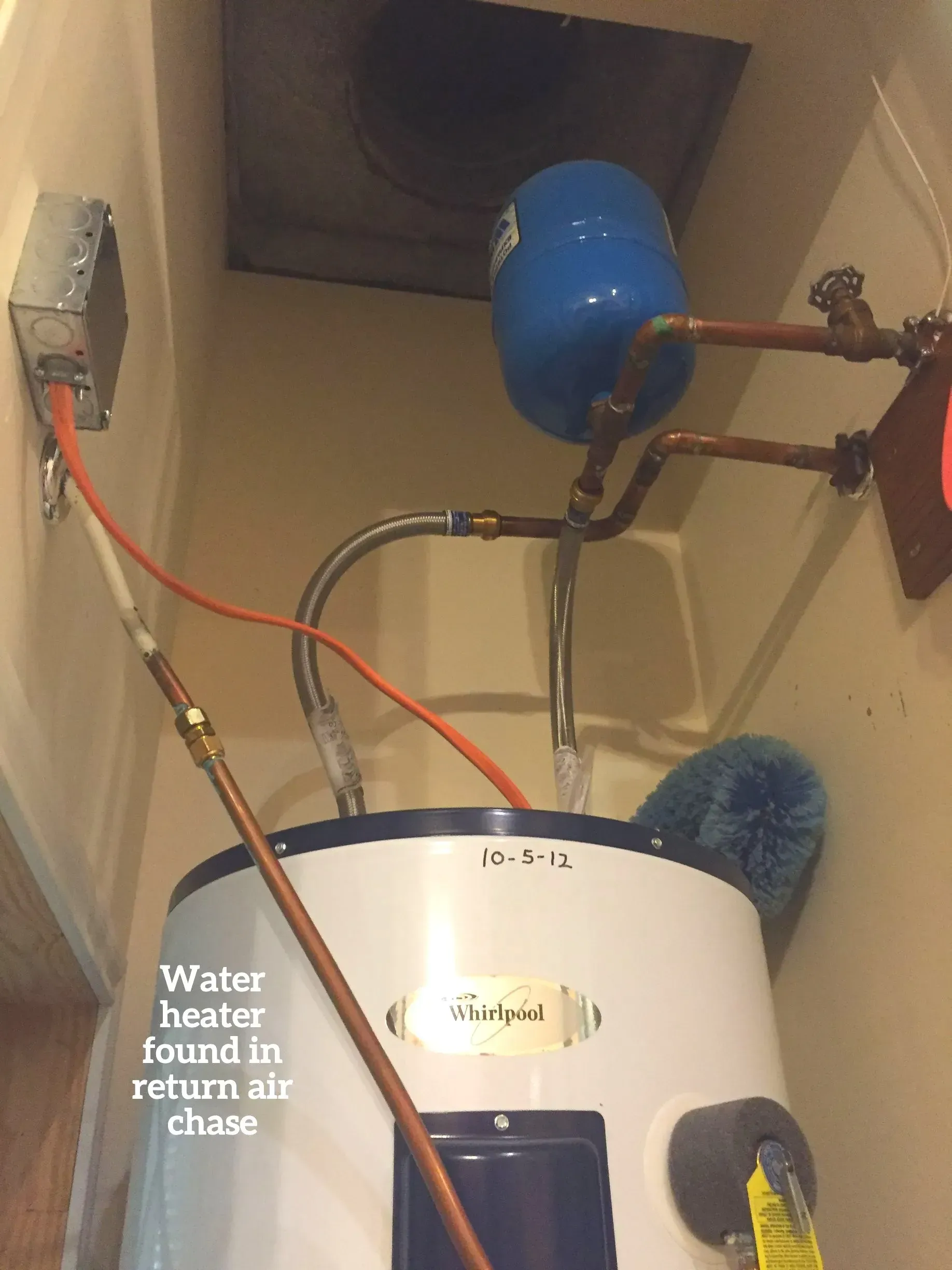 A white water heater with an attached blue expansion tank is improperly installed inside a return air chase.