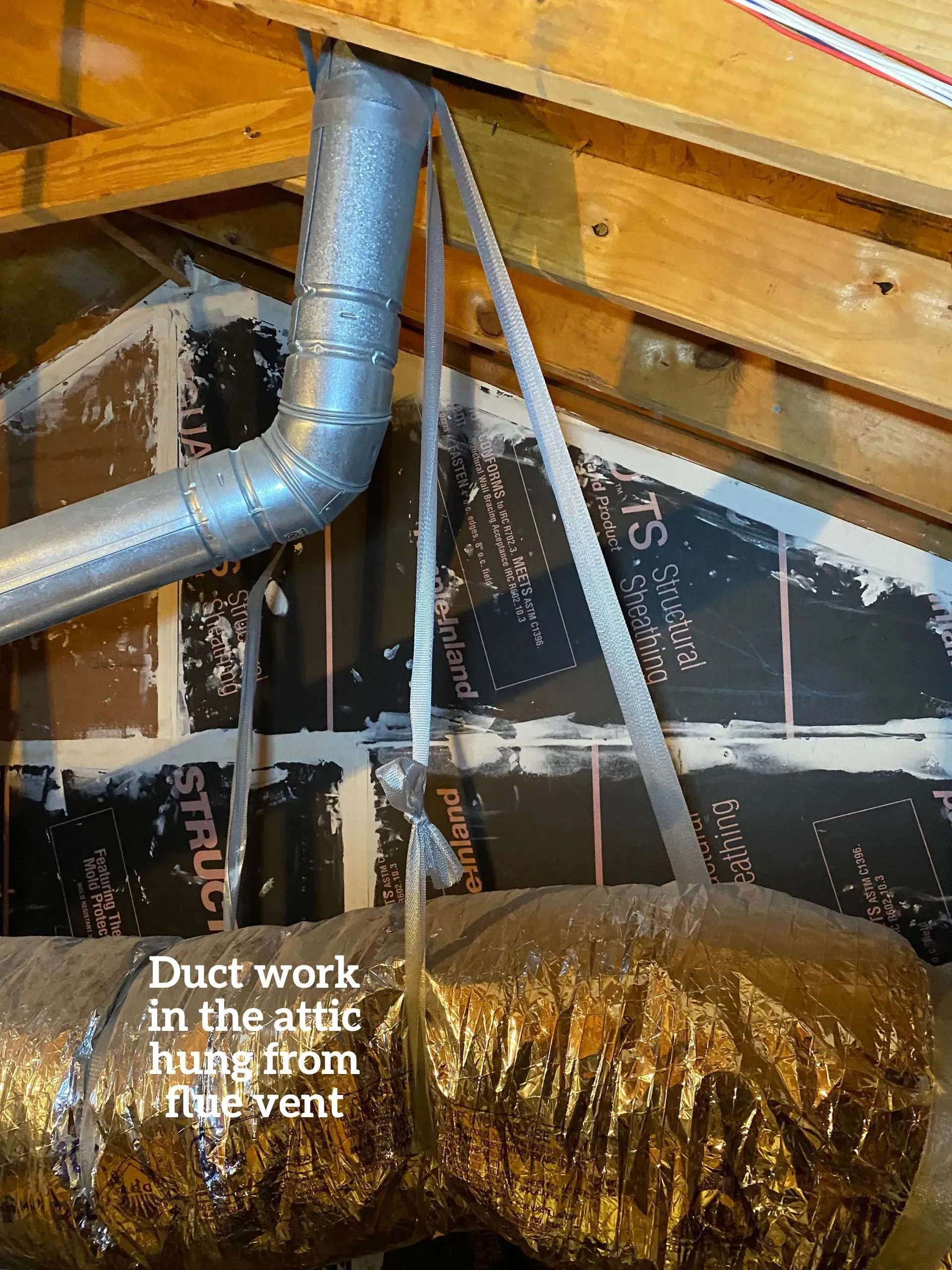 A flexible HVAC duct in an attic is improperly suspended using straps attached directly to a metal flue vent pipe.