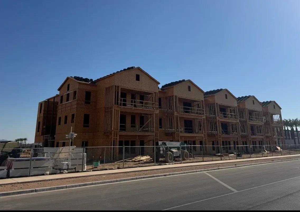 A multi-story residential building under construction with exposed wooden framing against a clear blue sky.