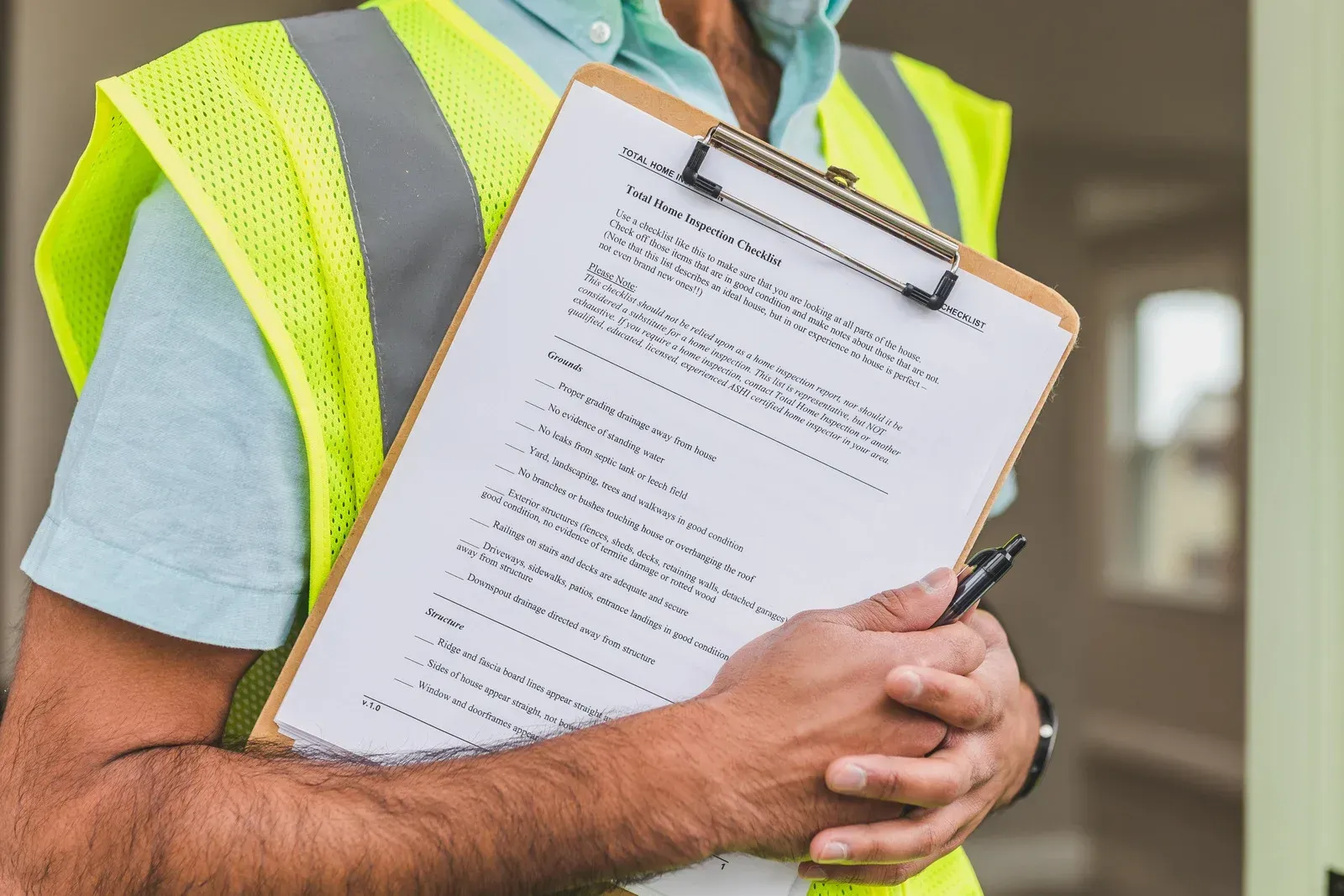 A person wearing a high-visibility vest holds a clipboard with a checklist while standing in a doorway.