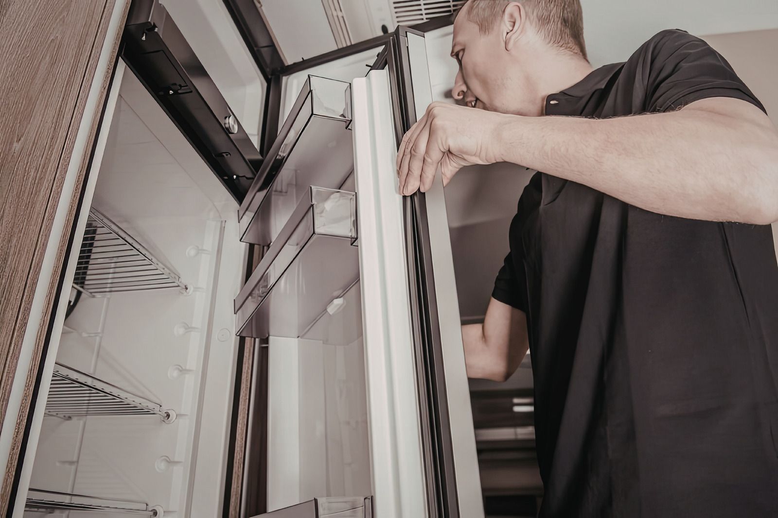A person in a black polo shirt inspects the door seal of a refrigerator.