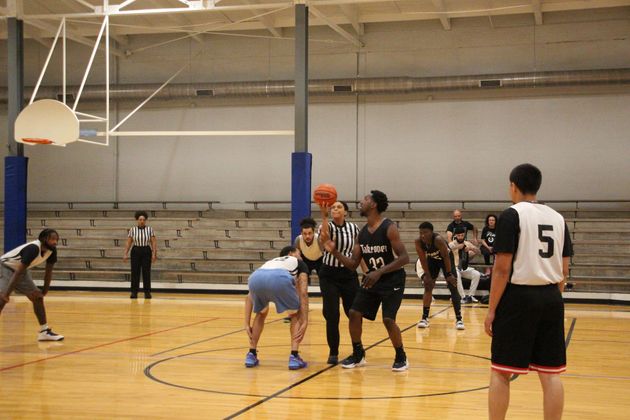 Basketball players and a referee prepare for a jump ball at center court in an indoor gymnasium.