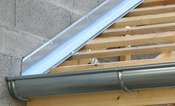 Section d'un toit en construction ; gouttière et solin métalliques installés sur des poutres 