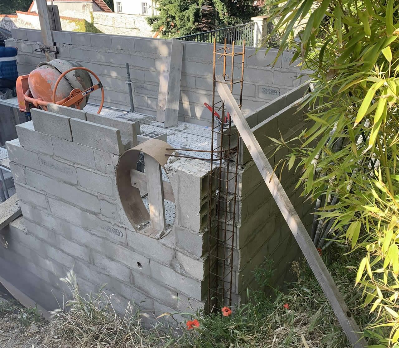 Chantier : murs en parpaings, armature en fer à béton, bétonnière, planche de bois.