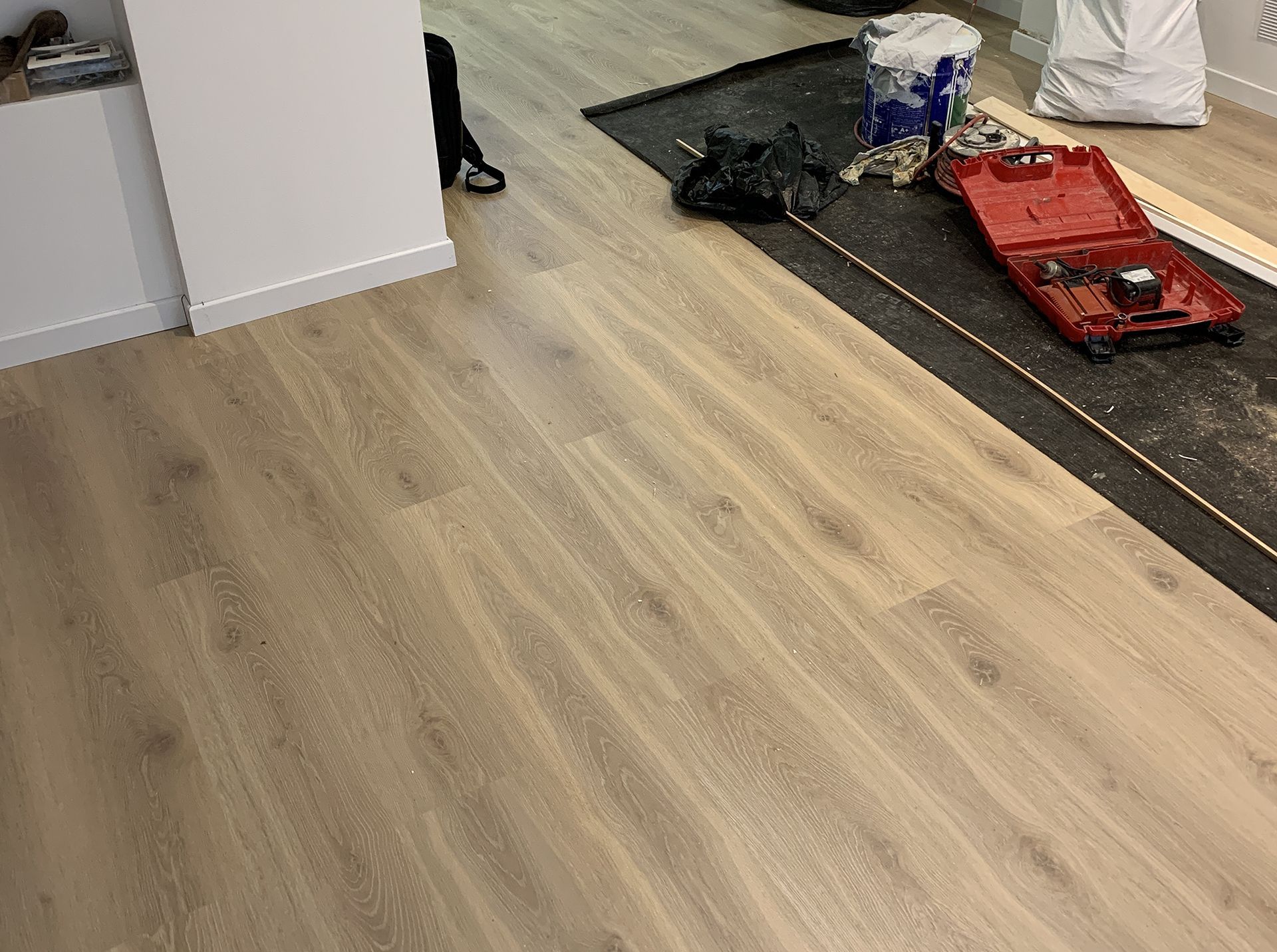 Plancher en bois avec outils de construction sur un tapis noir. Mur blanc à gauche.