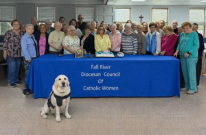 Group posing behind a blue banner reading “Fall River Diocesan Council of Catholic Women,” with a white dog in front