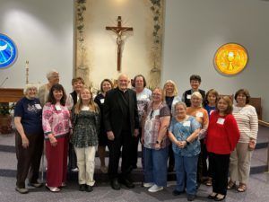 Group of people standing in a church beneath a large crucifix, facing the camera.