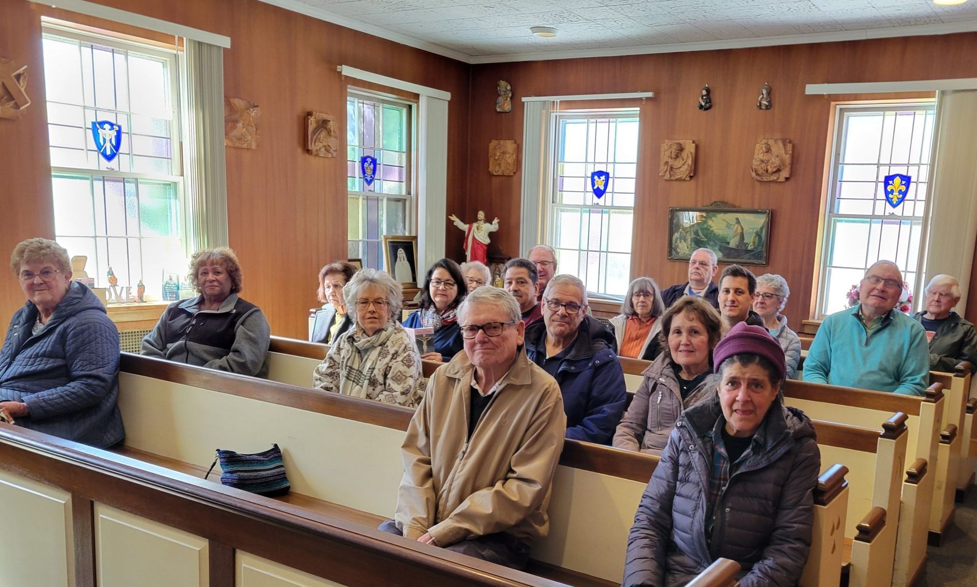 People seated in pews inside a wood-paneled church or meeting room, facing forward.